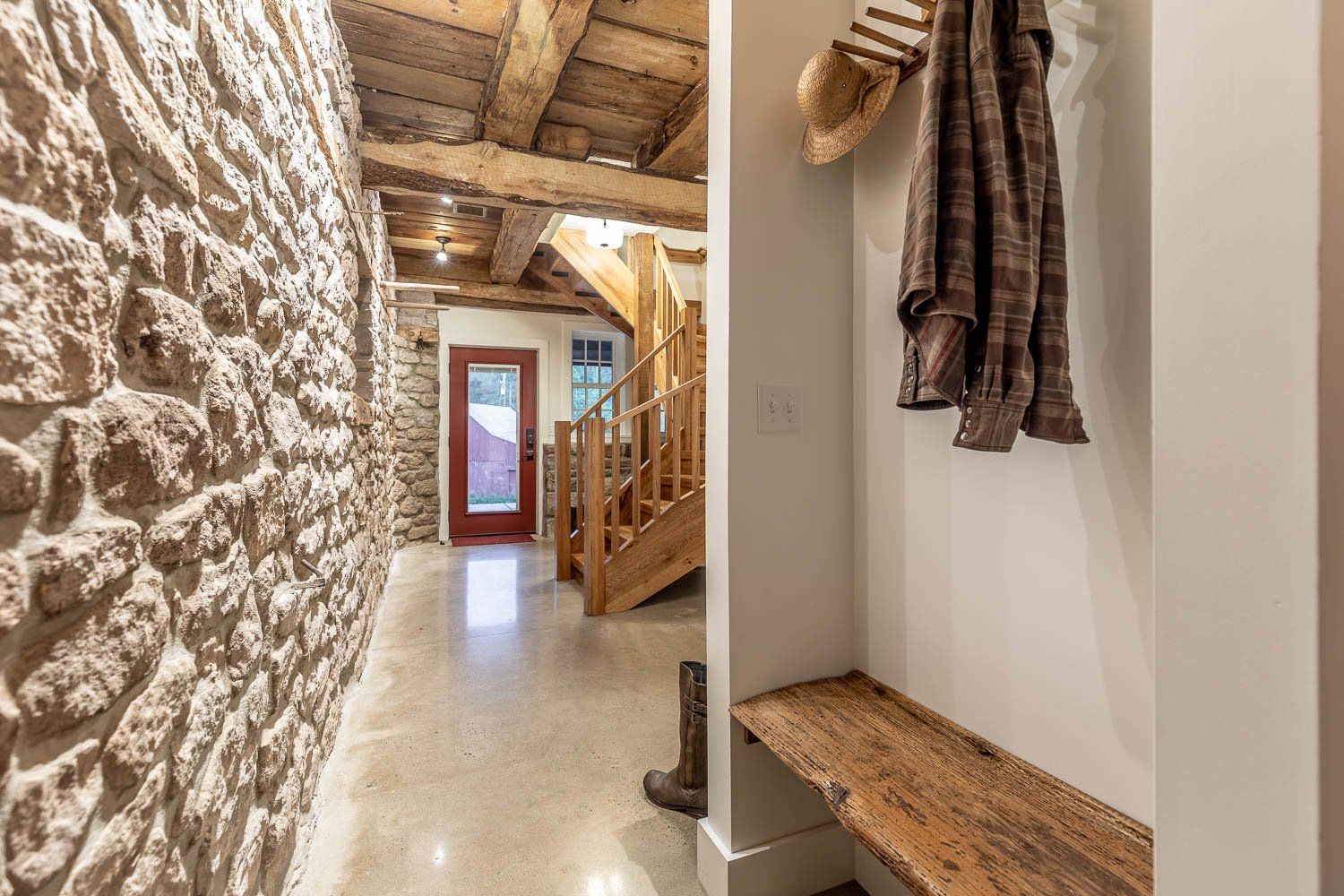 Stone wall hallway with wooden stairs and bench. Clothes and hat hang on wall.