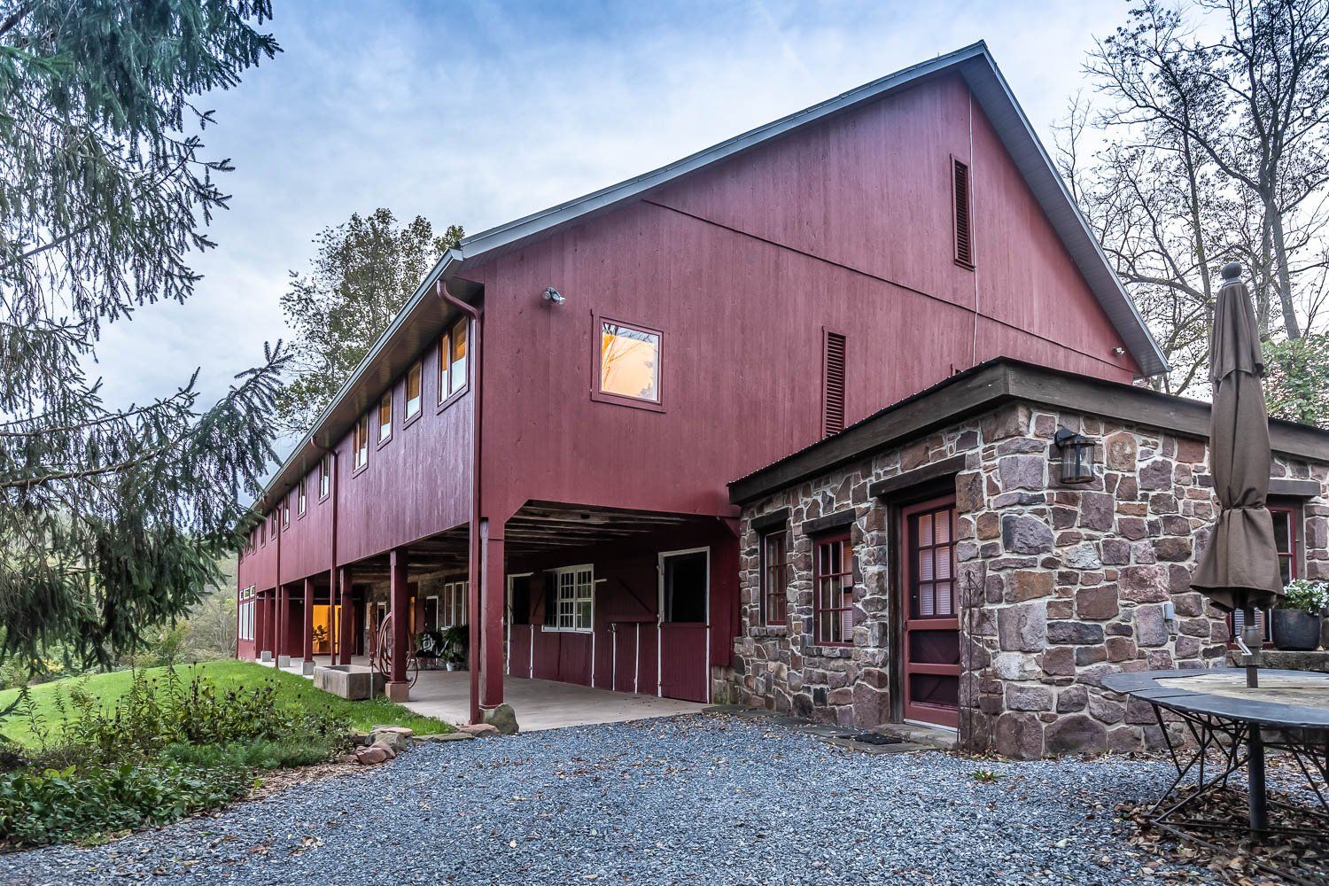Red barn with stone addition and covered walkway. Gravel driveway.