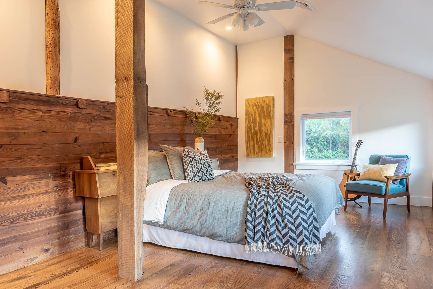 Bedroom with a wooden headboard, light blue bedding, and a sitting area with a guitar by a window.
