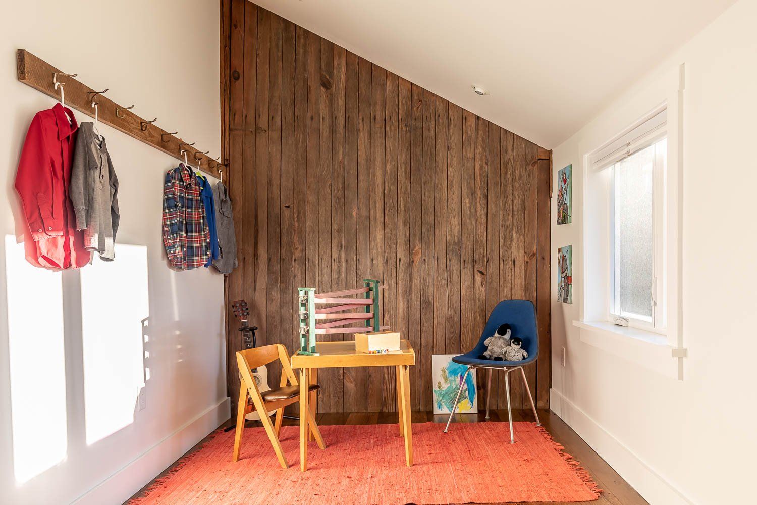 Cozy play area with wood accent wall, small table, colorful rug, and hanging coats.