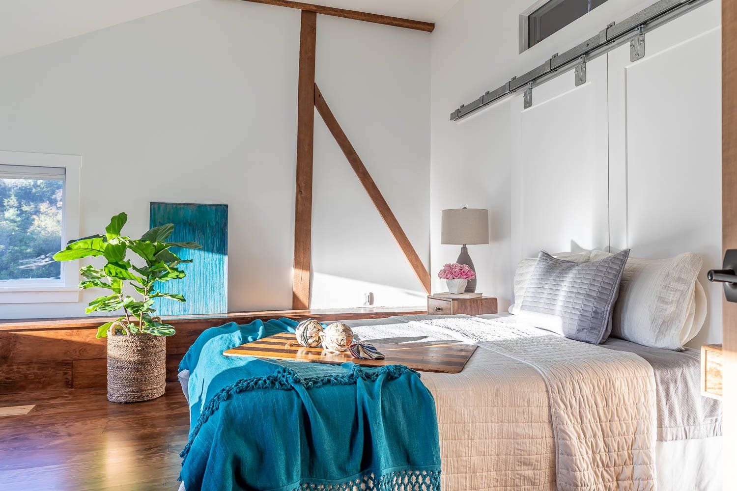 Bedroom with white walls, wooden beams, a bed with a teal blanket, and a potted plant.