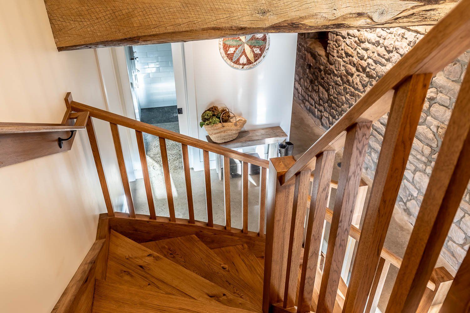 Wooden staircase leads to a hallway with a rustic stone wall and a table with flowers.