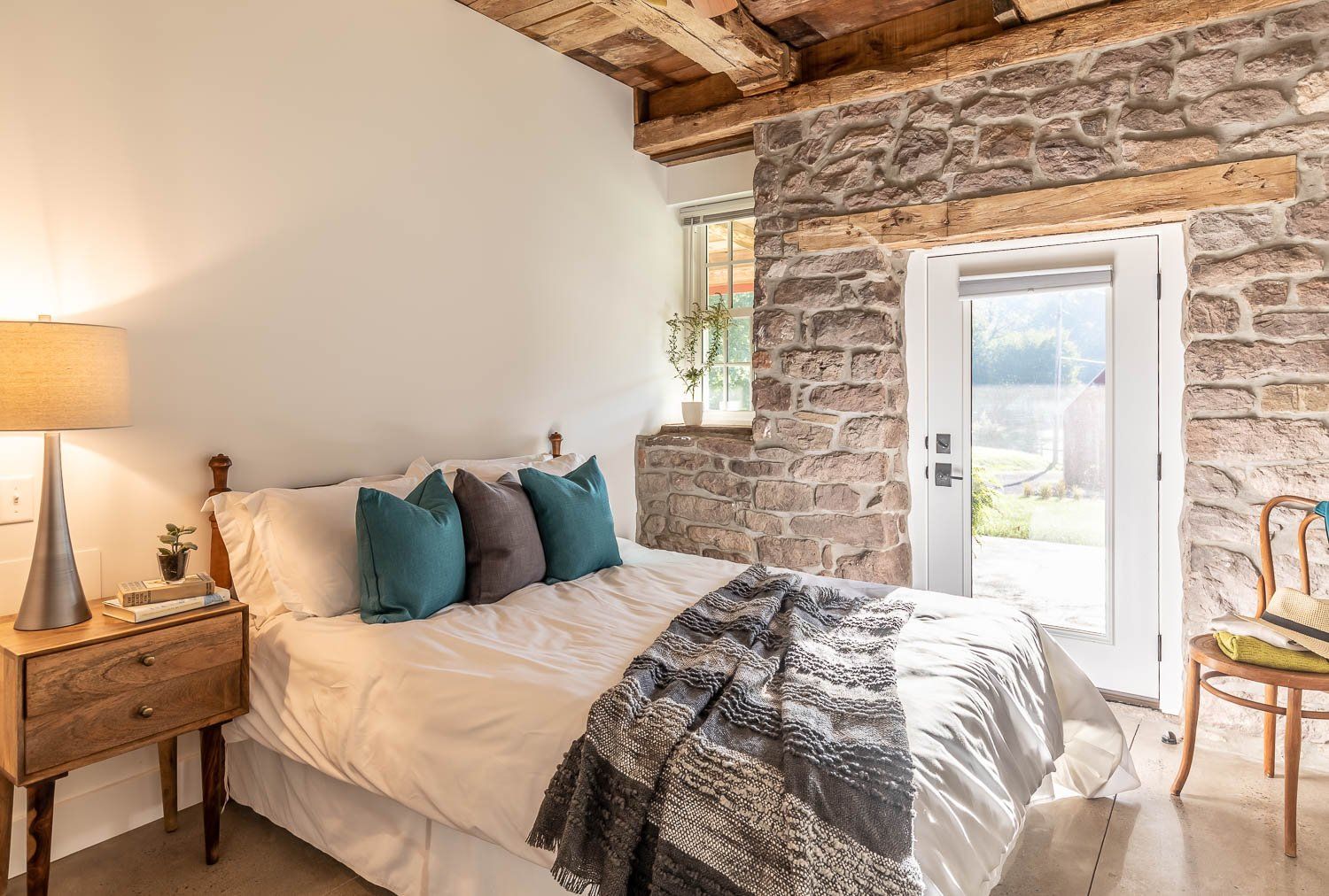 Bedroom with stone wall, bed, nightstand, and doorway leading outside.