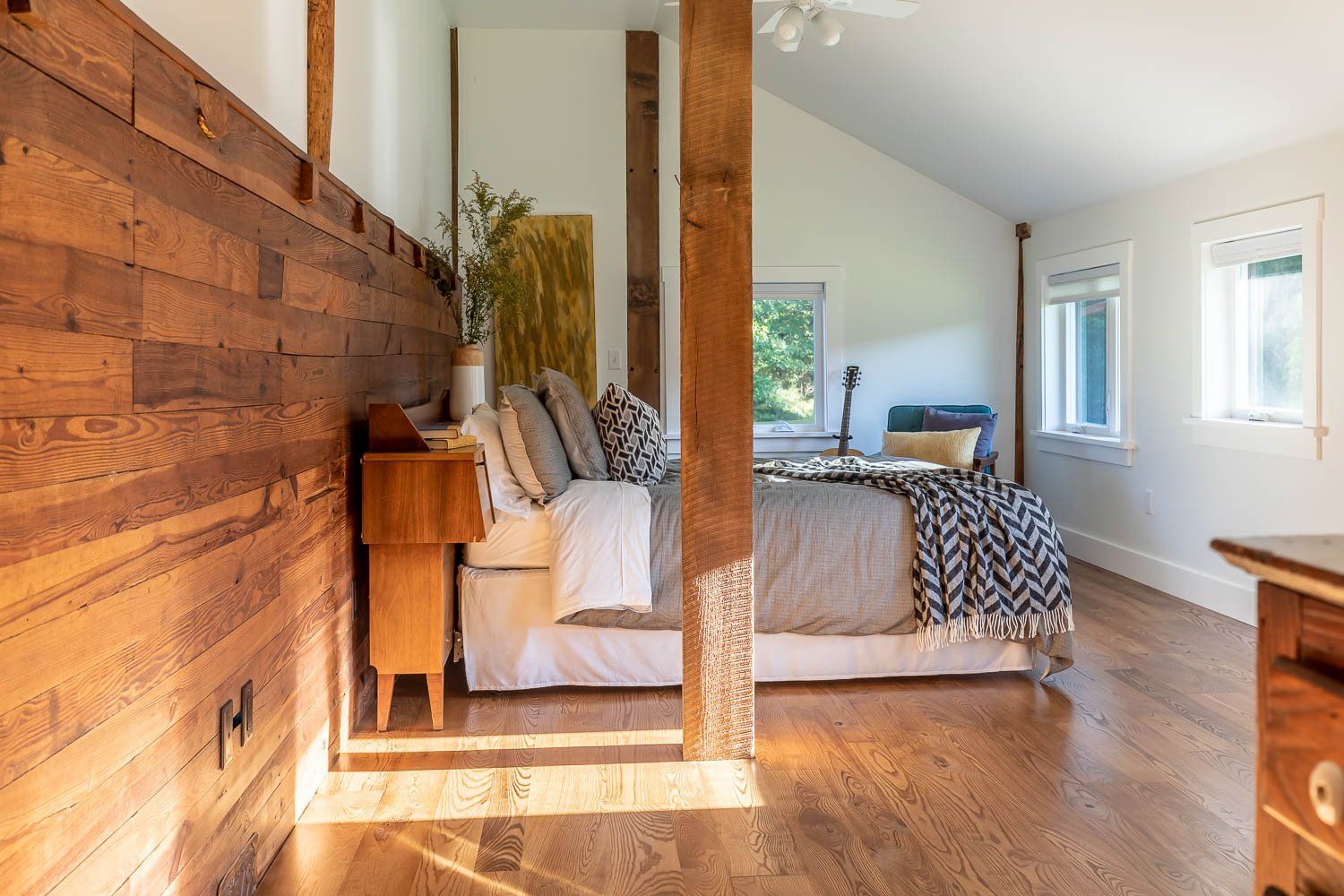 Bedroom with wood paneling, hardwood floors, bed with decorative pillows, and a window.