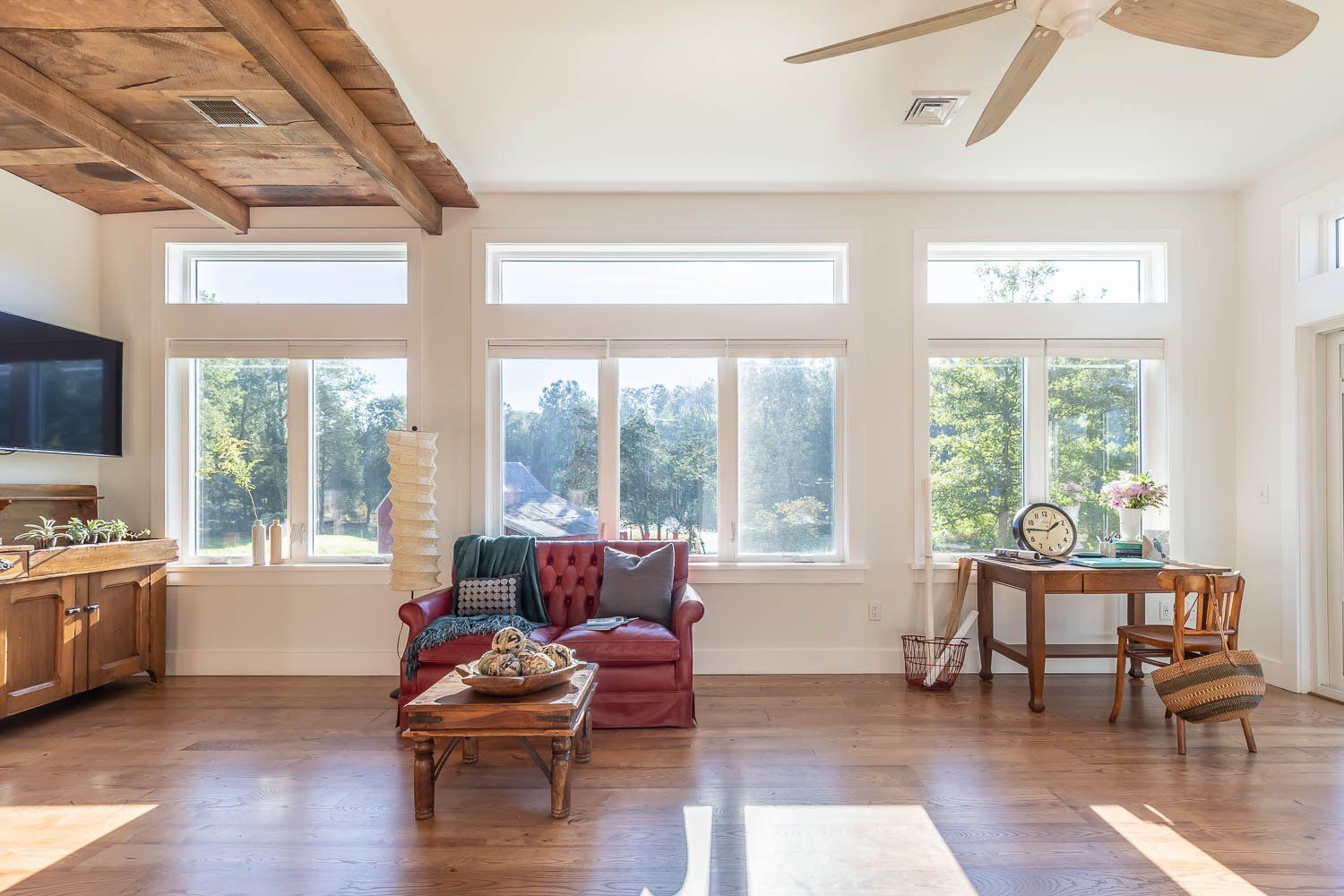 Spacious living room with red sofa, wooden furniture, large windows, and exposed wooden beams.
