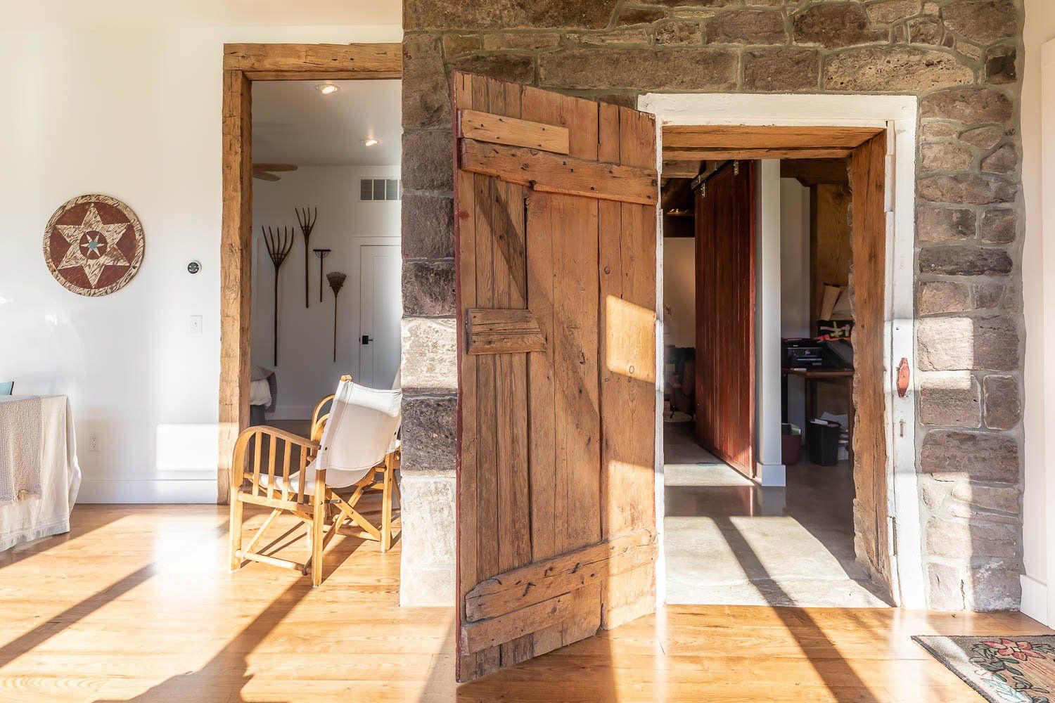 Wooden door ajar in stone doorway, revealing a view into bright room with chair and artwork.