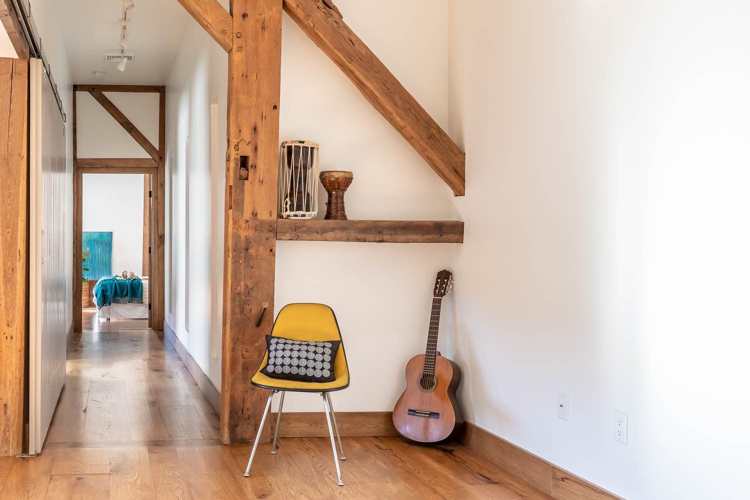 Hallway with wooden beams, yellow chair, guitar, and decorative items.