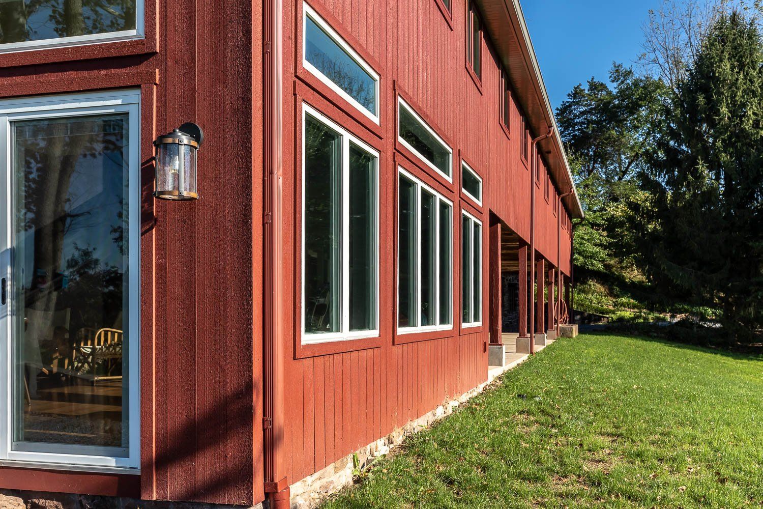 Red-sided building with white-framed windows, built on a raised foundation. Green grass in foreground, trees in background.