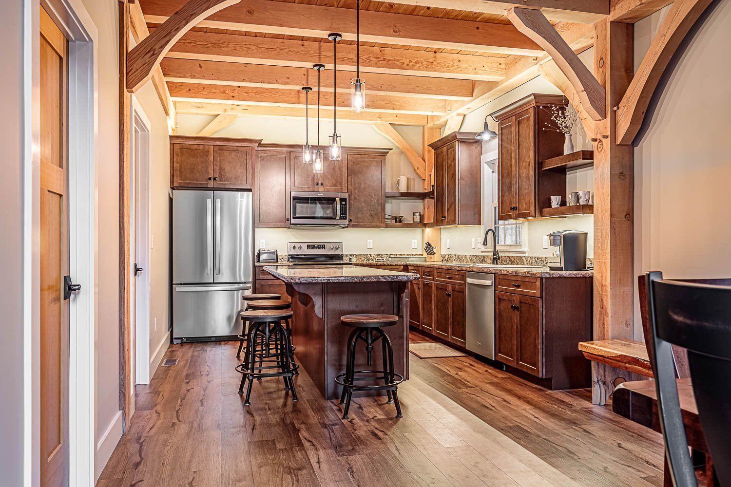 Kitchen with wooden beams, dark cabinets, stainless steel appliances, island with stools.