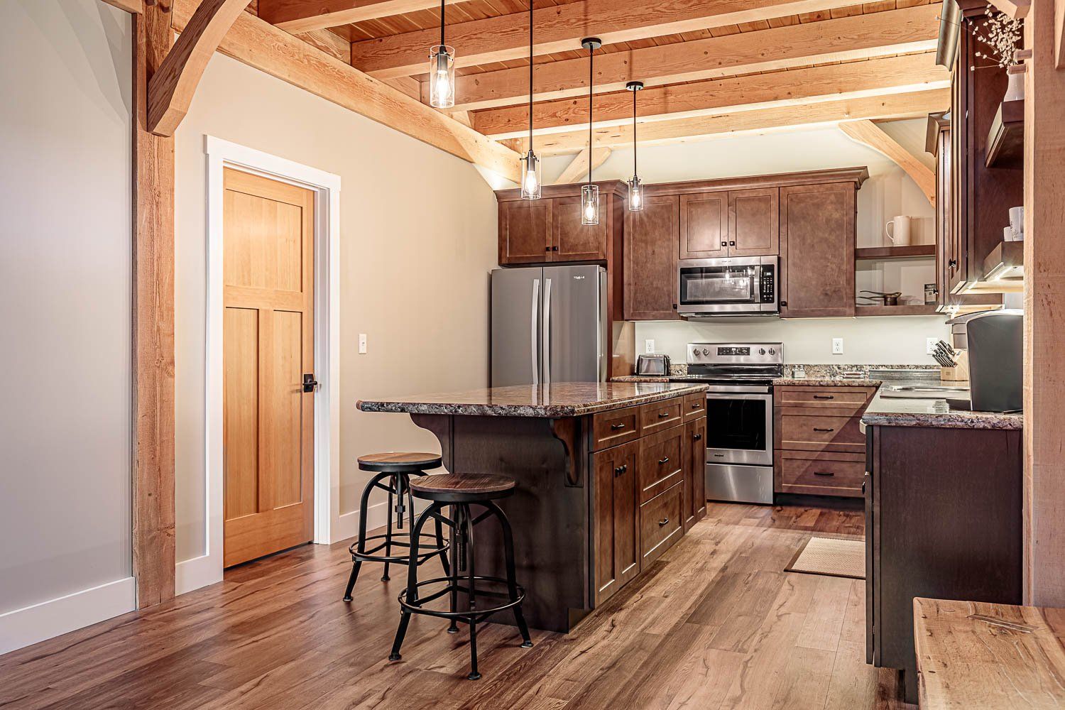 Kitchen with wood beams, dark cabinets, island with stools, and stainless steel appliances.