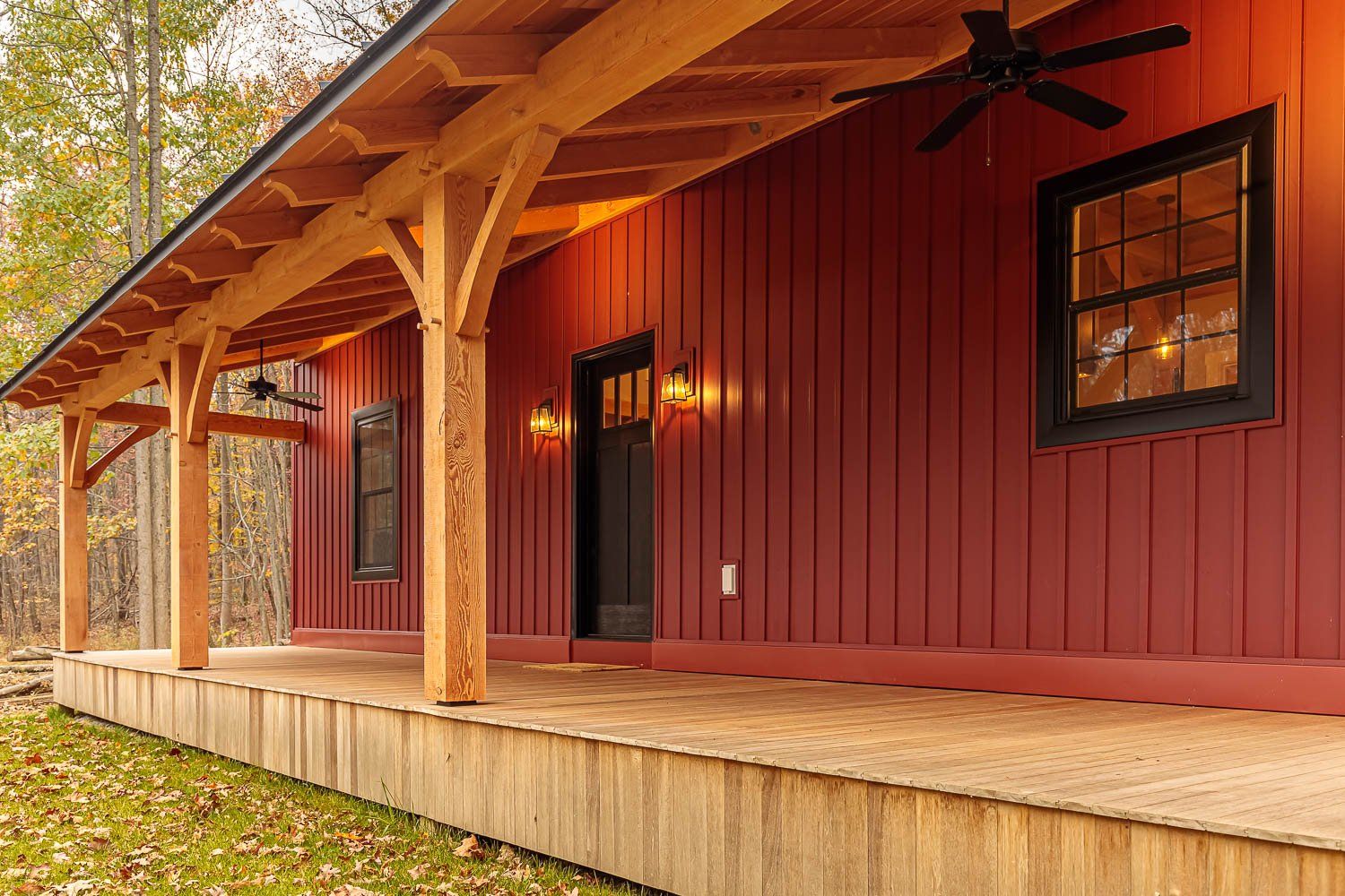 Red wooden cabin with porch, brown beams, black windows and door, and ceiling fan.