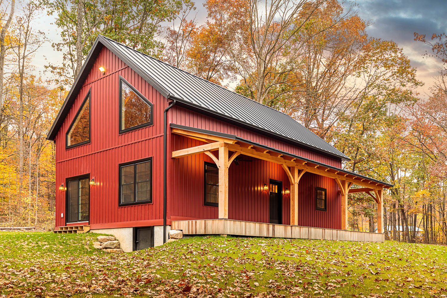 Red barn-style building with black trim and a porch, set in an autumn landscape with colorful trees.