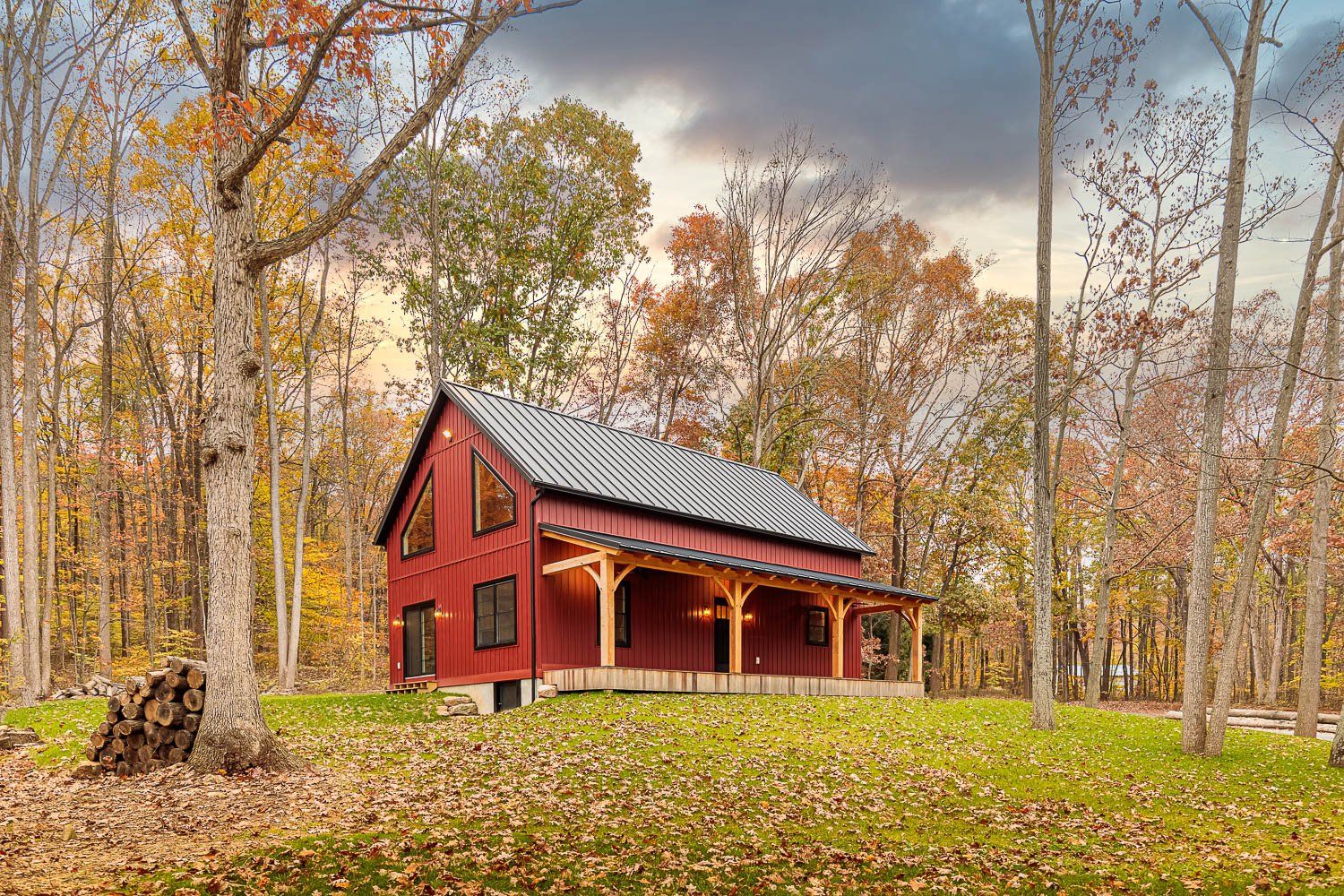 Red barn-style house with black roof, surrounded by fall foliage on a grassy hill.