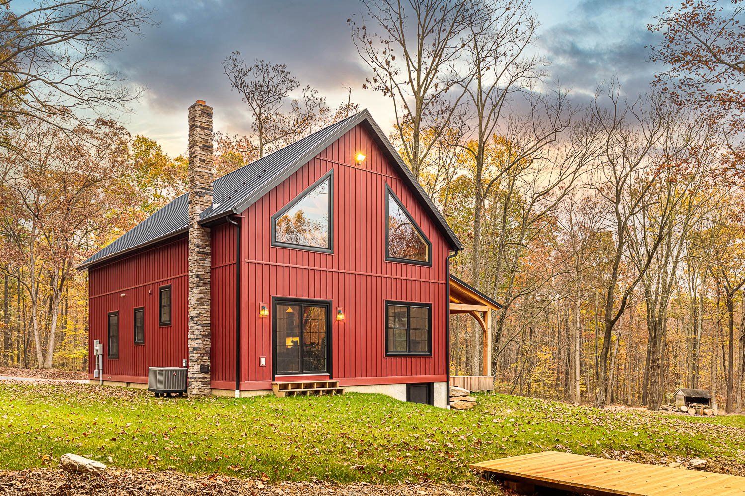 Red cabin with black trim and chimney in a wooded area with fall foliage.