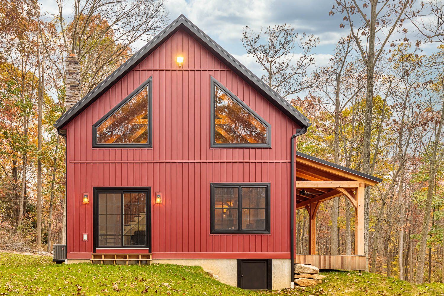 Red barn-style house with triangular windows and a porch, set in an autumn forest.