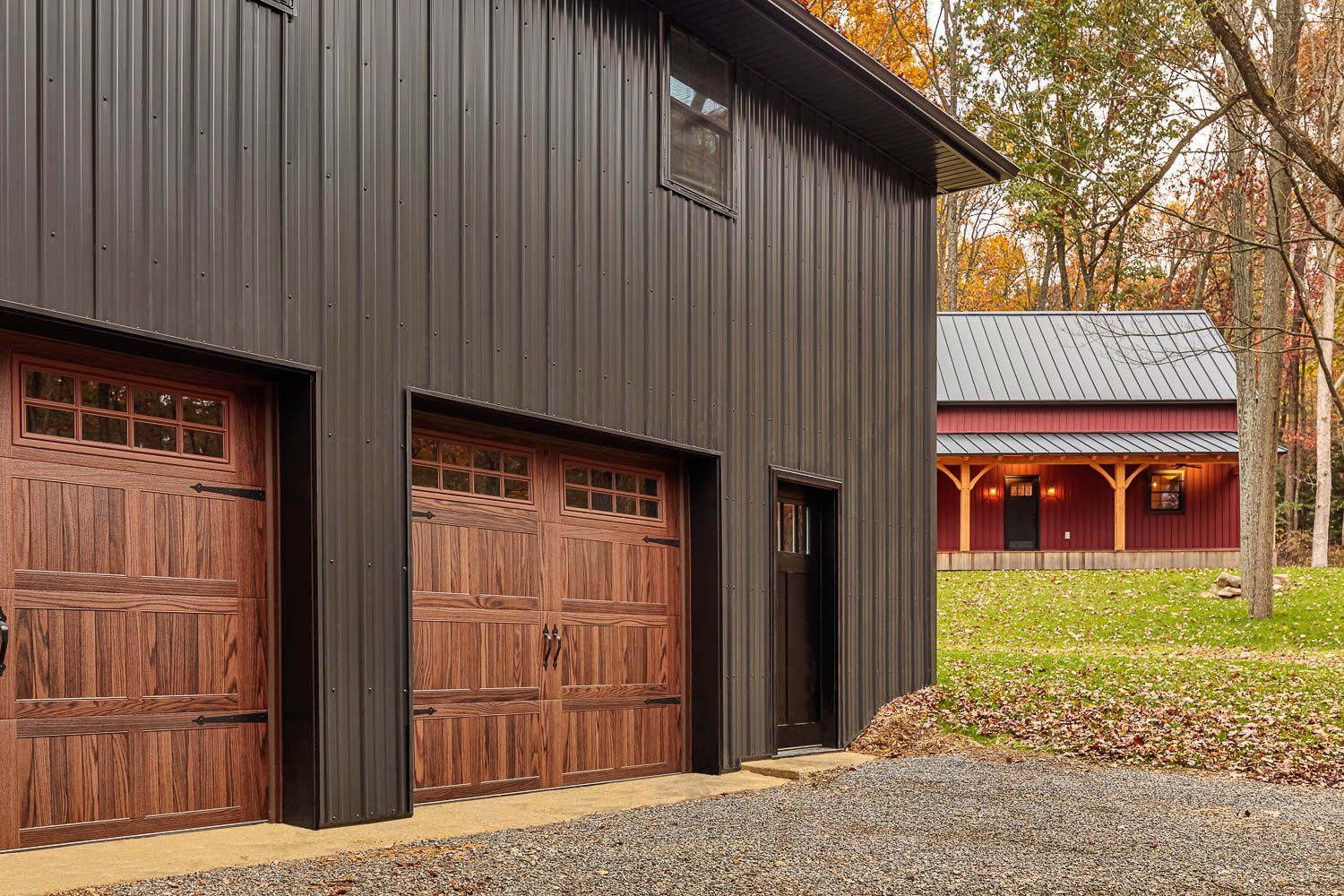 Dark gray metal-sided garage with wooden garage doors. Red building visible in background.