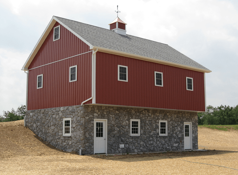 Red and stone two-story barn with windows, on a slightly elevated hillside.