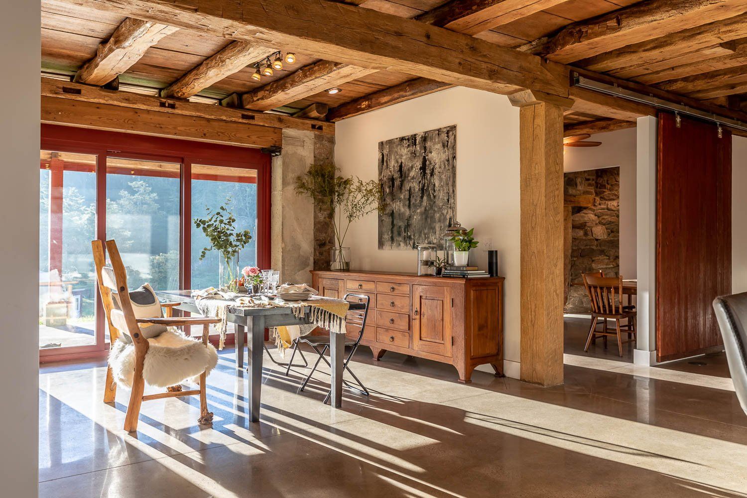 Dining room with wooden beams, table set for meal, natural light, artwork on wall.