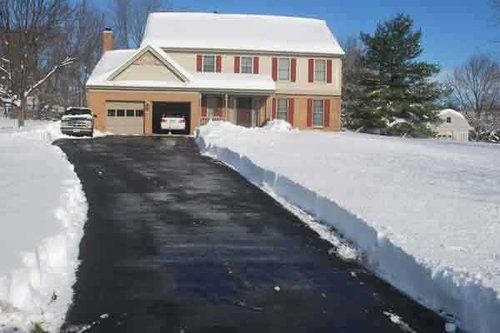 Two-story house with cleared driveway. Snow on roof and lawn, cars in driveway and garage.