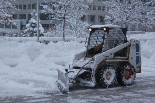 White Bobcat snowplow clearing snow from a parking lot on a snowy day.