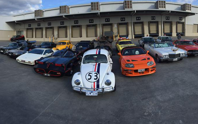 A bunch of cars are parked in front of a building and one of them has the number 53 on it