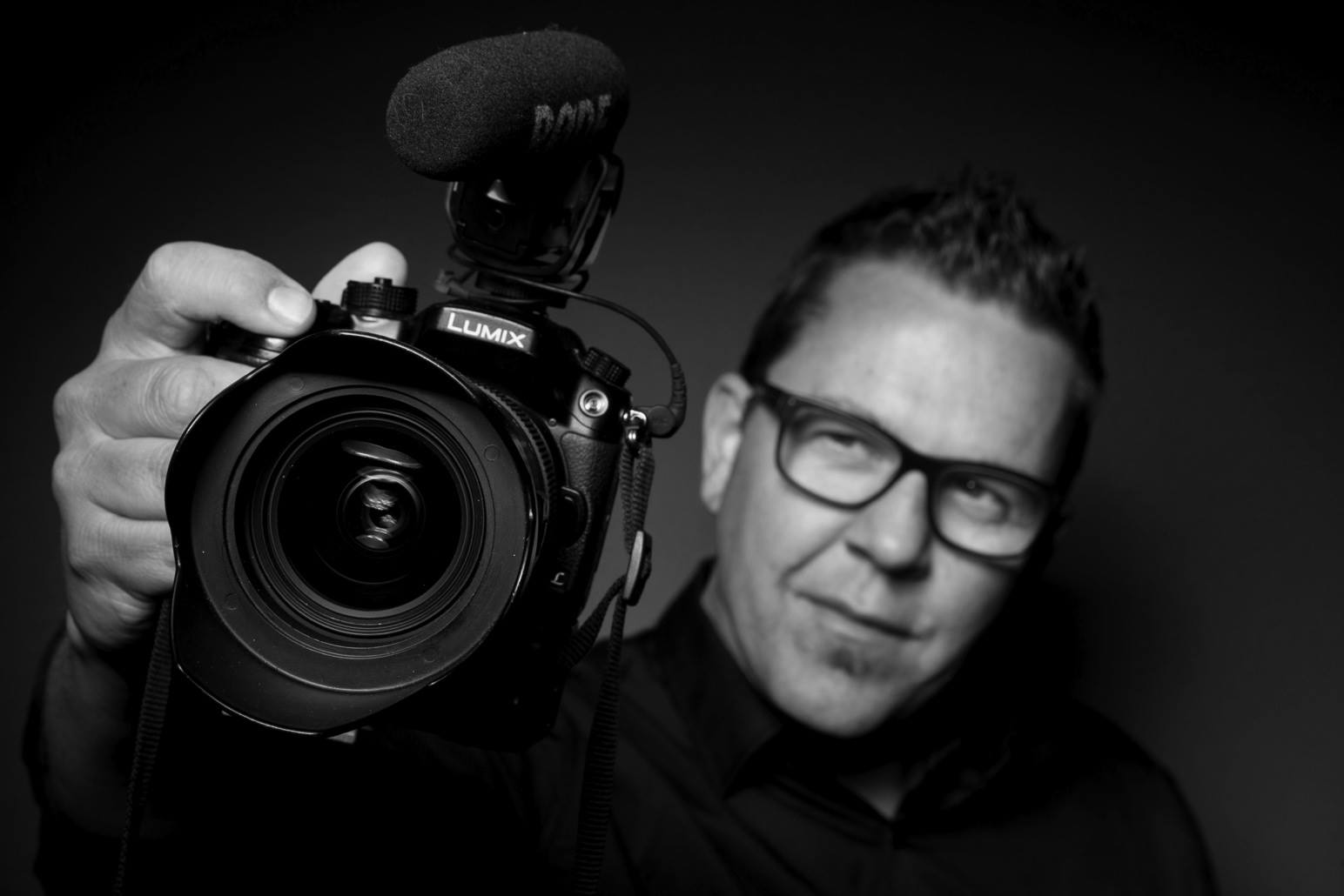 A man wearing glasses is holding a rode camera