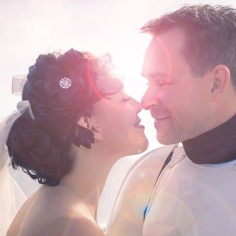 A bride and groom are kissing in front of the sun.