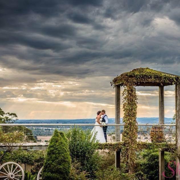 A bride and groom are kissing on a balcony overlooking a city.