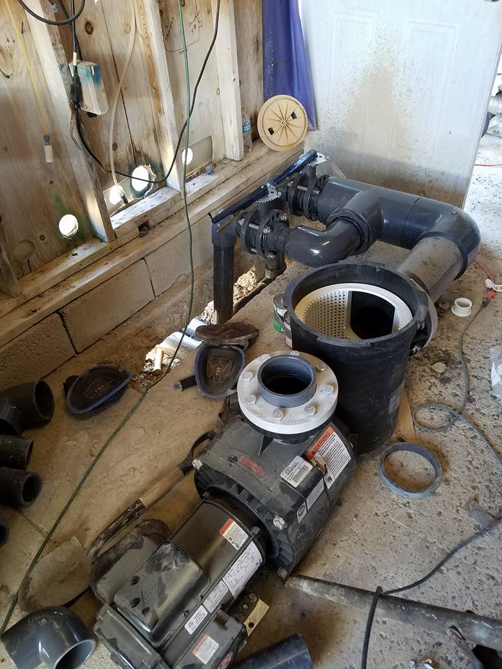 Pool pump components, pipes, and electrical box scattered on a concrete surface, likely during repair or installation.