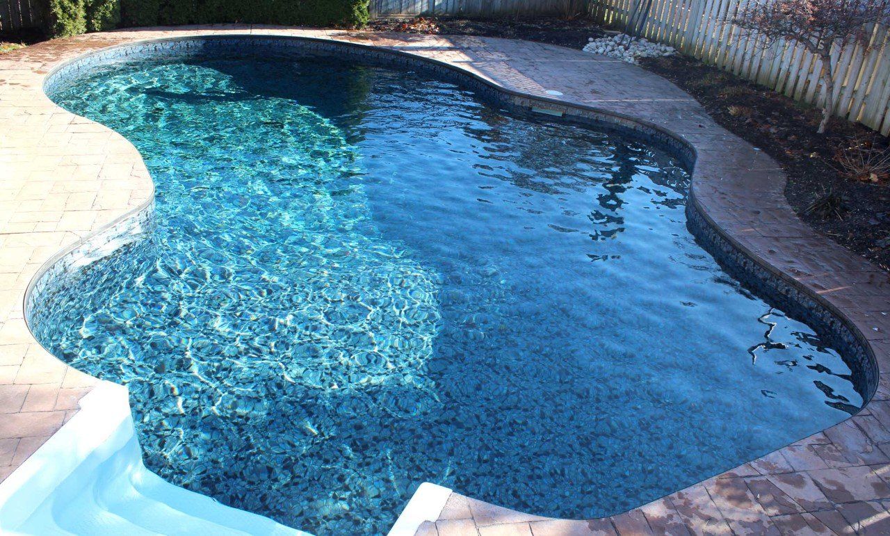 Pool with turquoise water, surrounded by brick patio, in an outdoor setting.
