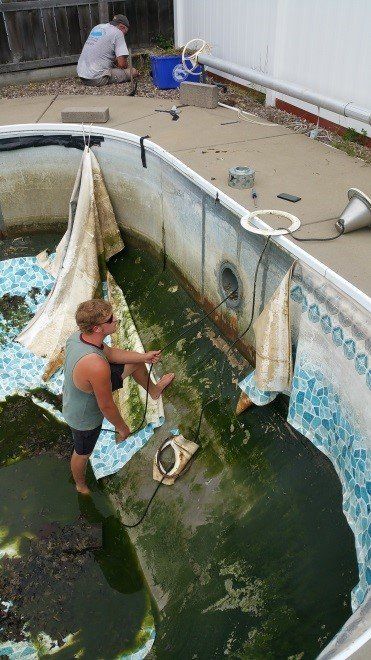 Man standing in a dirty pool, removing the liner. Another man works outside the pool.