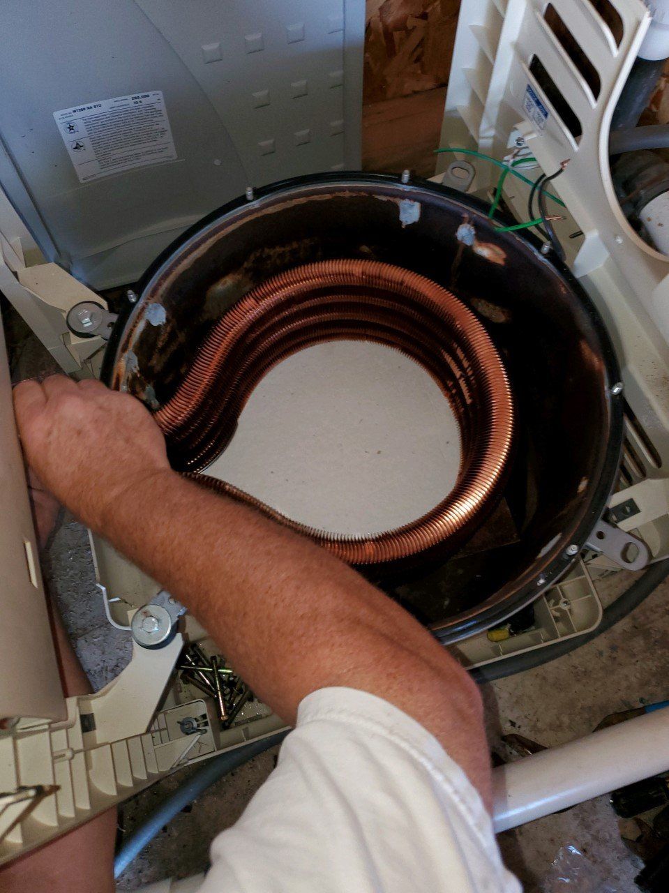 A person's hand removing a copper coil from a washing machine drum.