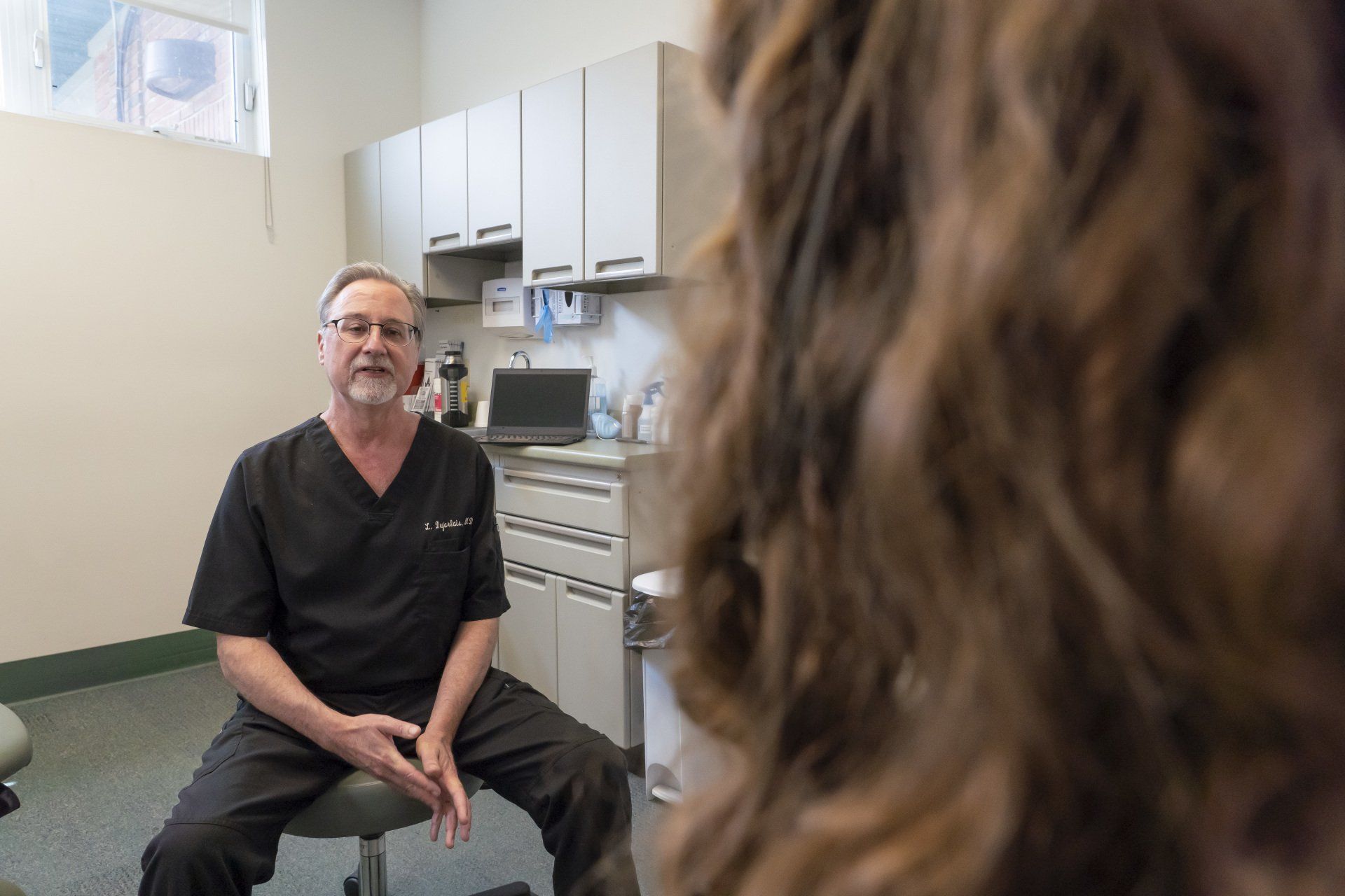 Dr. Desjarlais sitting on a stool in a room talking to a patient