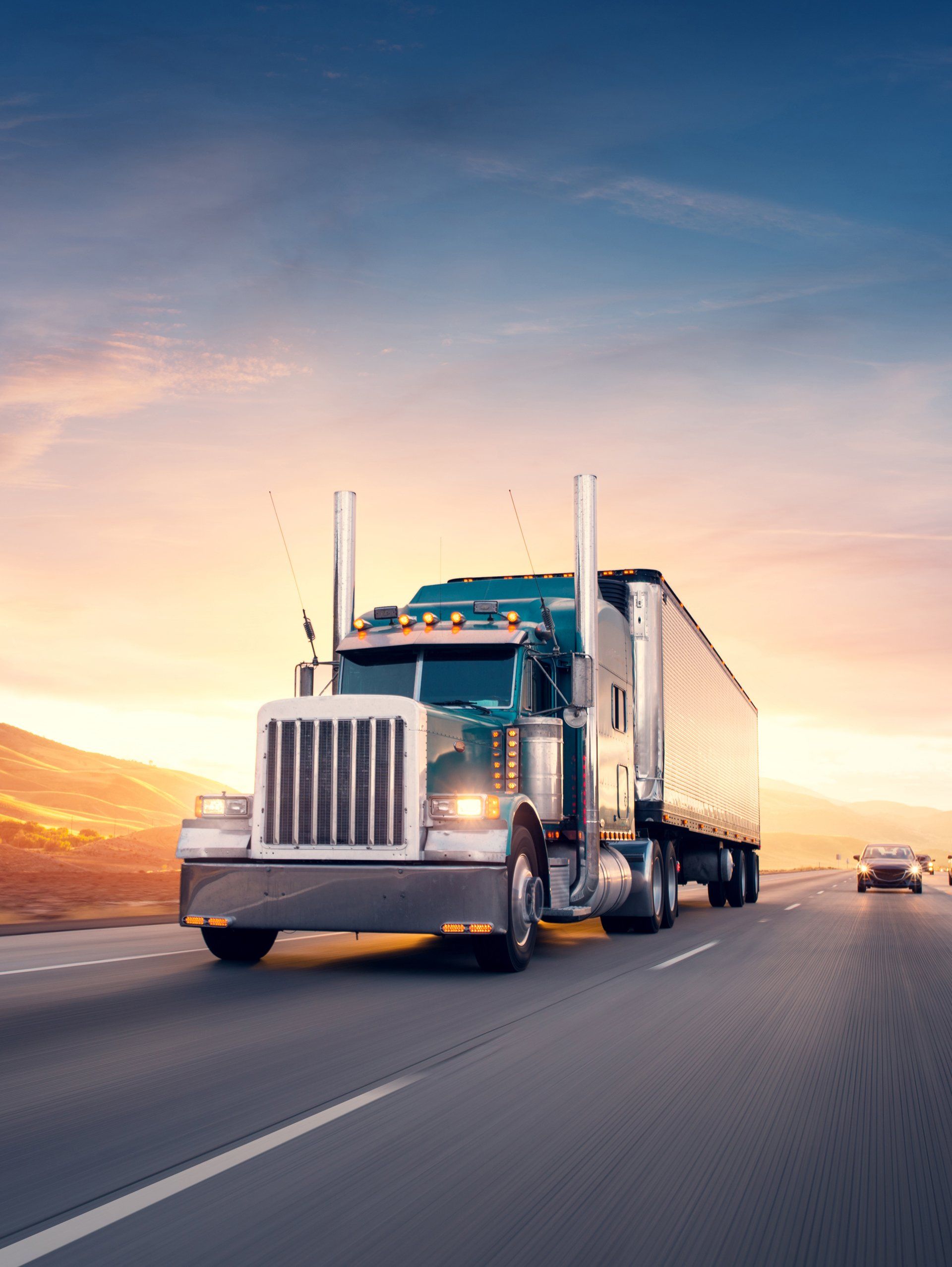An American style truck is driving down a highway at sunset