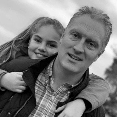 A man is carrying a little girl on his shoulders in a black and white photo.