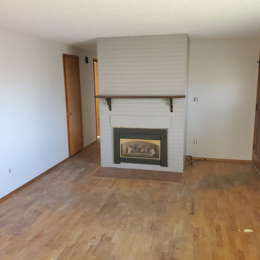 After image of a living room with a newly white-painted fireplace, fresh white walls, and warm wood floors. 