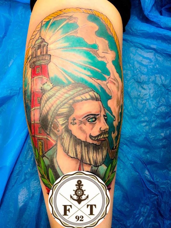 Ein Tattoo eines bärtigen Mannes mit einem Leuchtturm im Hintergrund