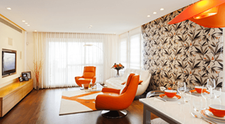 A TV room with orange leather tub chairs, orange crockery and orange lamp over the table, and feature wall decorated with palms