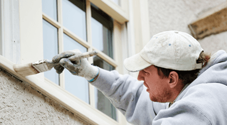 A man in a white cap, painting a window frame white