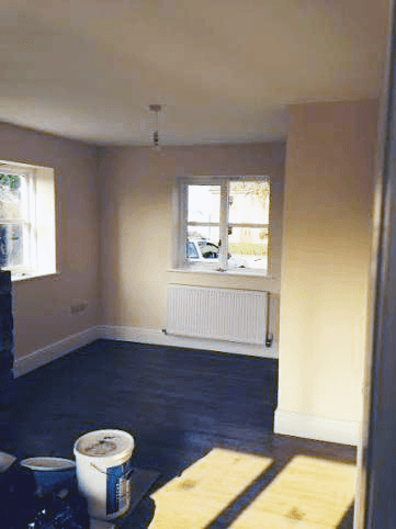 An empty room with pale walls, dark floor and two windows