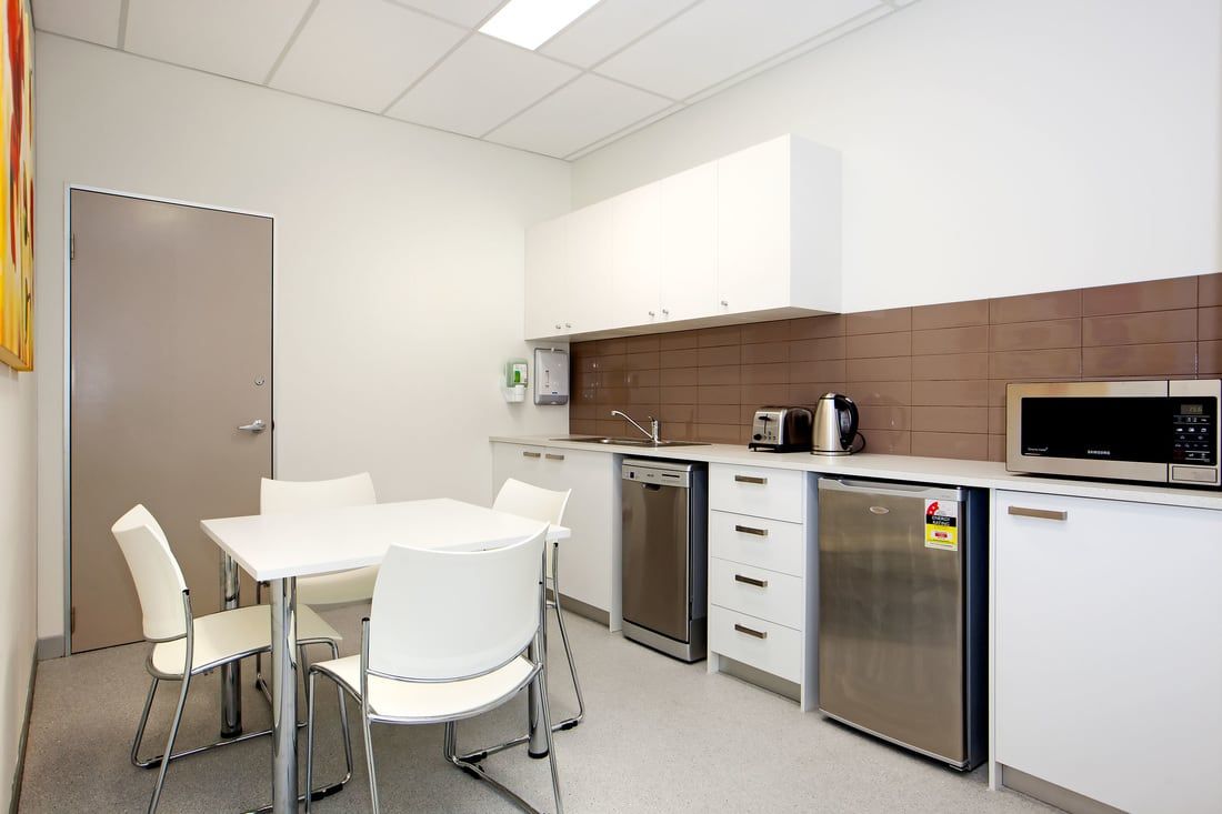 Small office kitchenette with white table, chairs, cabinets, sink, microwave, dishwasher, and coffee maker.