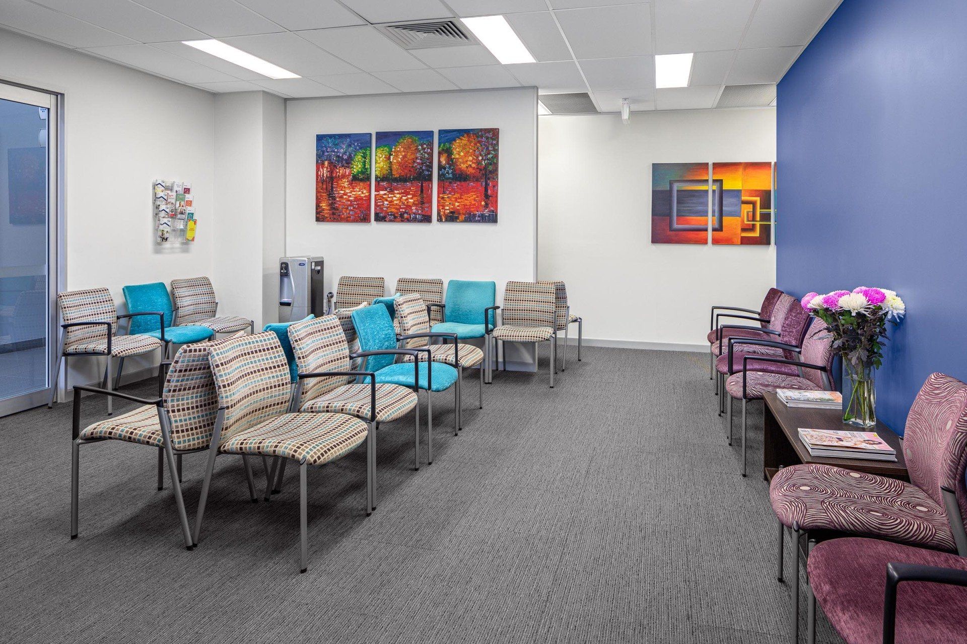 Modern waiting room with patterned chairs, colorful wall art, and gray carpet