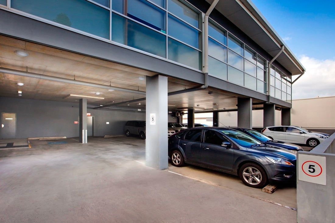 Covered parking lot with several parked cars and a modern building above