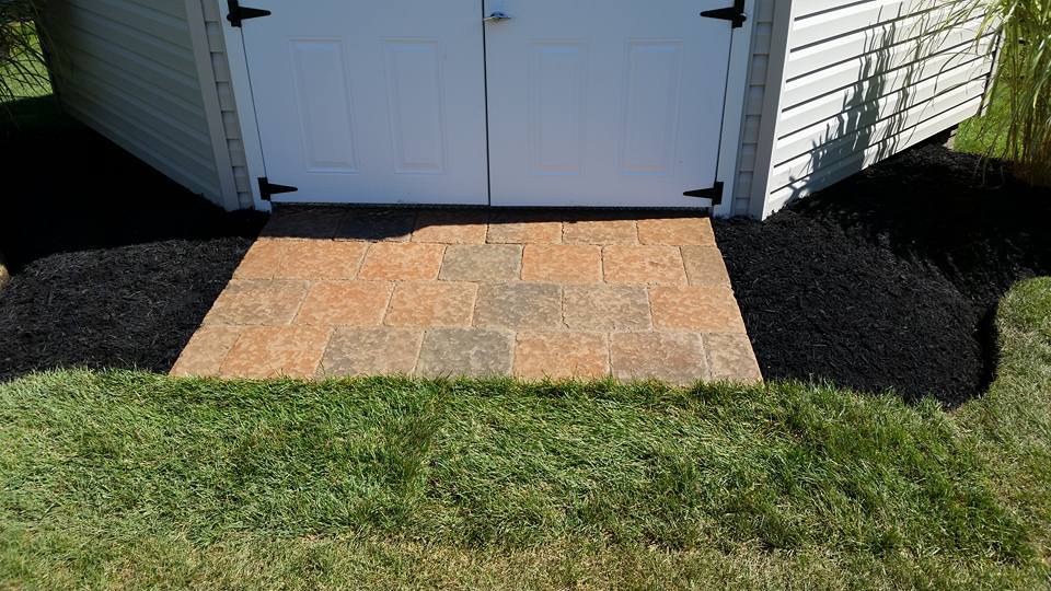 a white shed with a brick walkway leading to it .