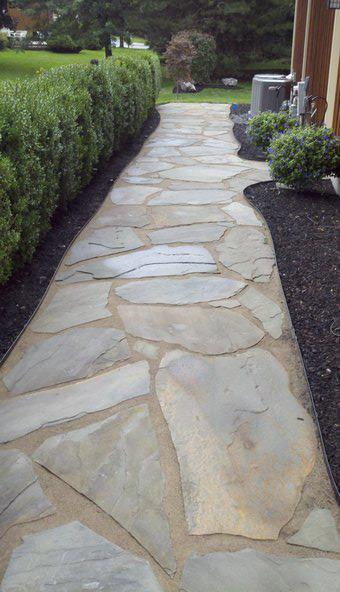 a stone walkway leading to a house with a hedge in the background .