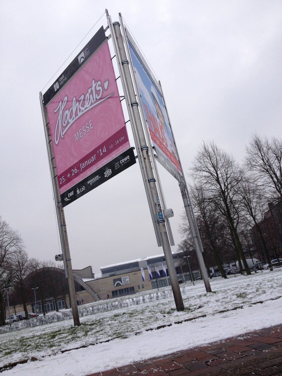 Rosa und blaue Banner für „Tickets“ auf einem Metallrahmen vor einer verschneiten Landschaft.