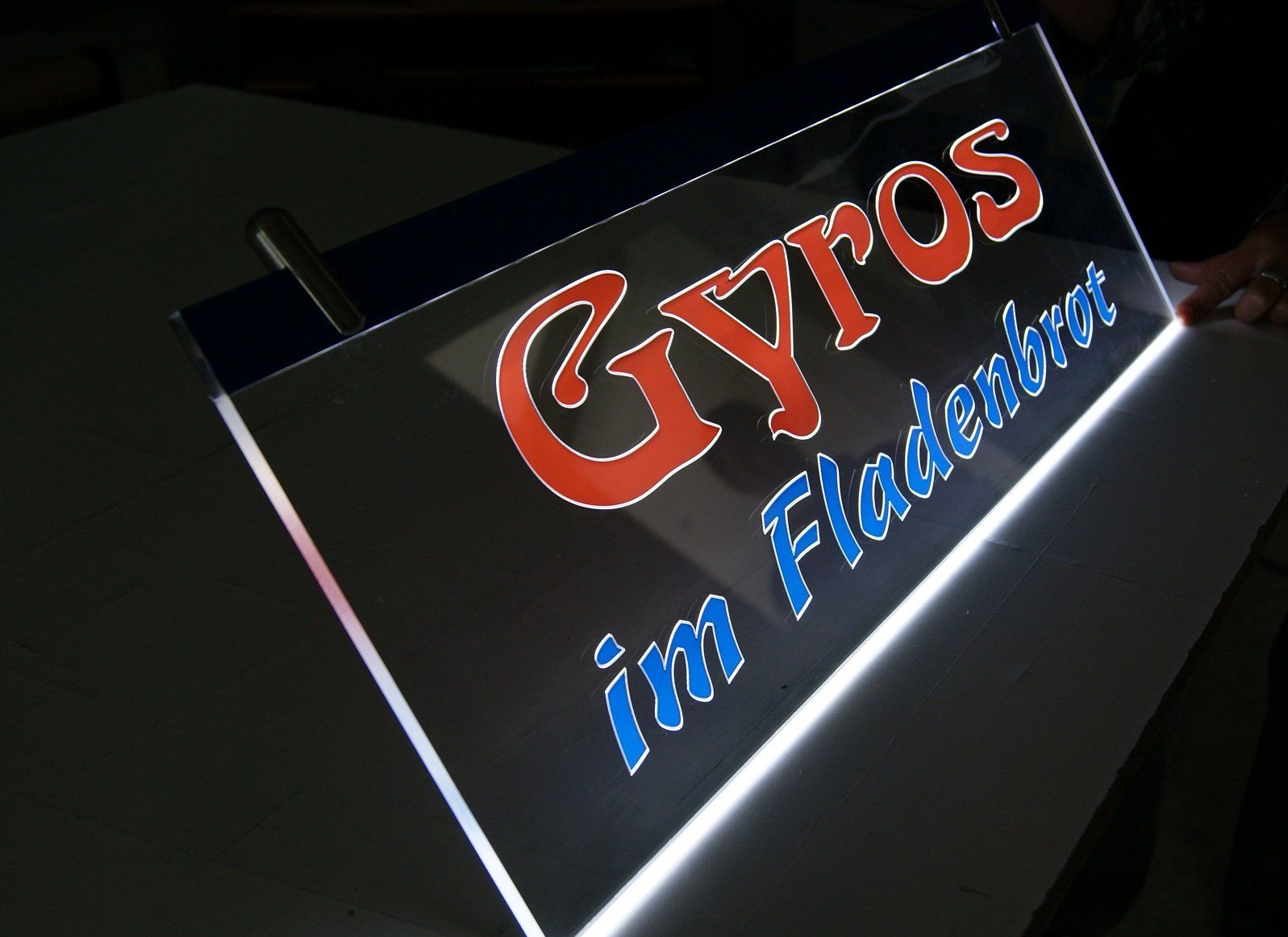 Leuchtschild: „Gyros im Fladenbrot“ in Rot und Blau auf einer transparenten Platte.
