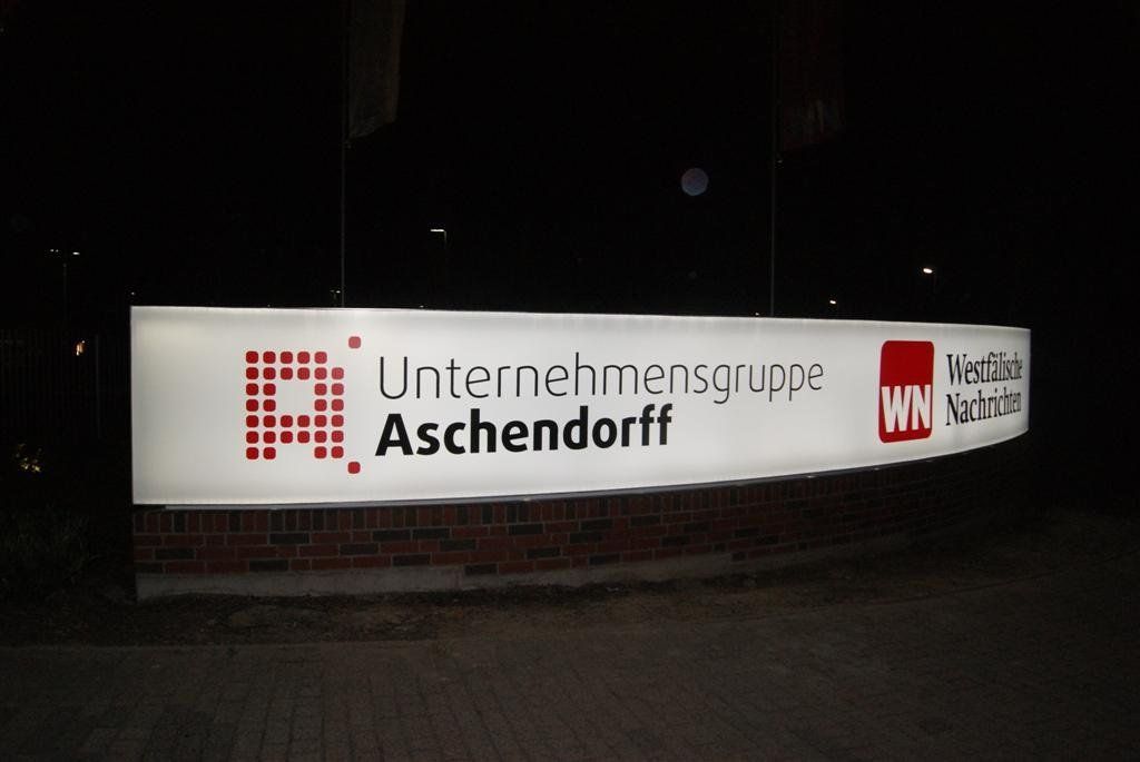 Leuchtschrift bei Nacht: „Unternehmensgruppe Aschendorff“ in Weiß mit rot-weißen Logos.