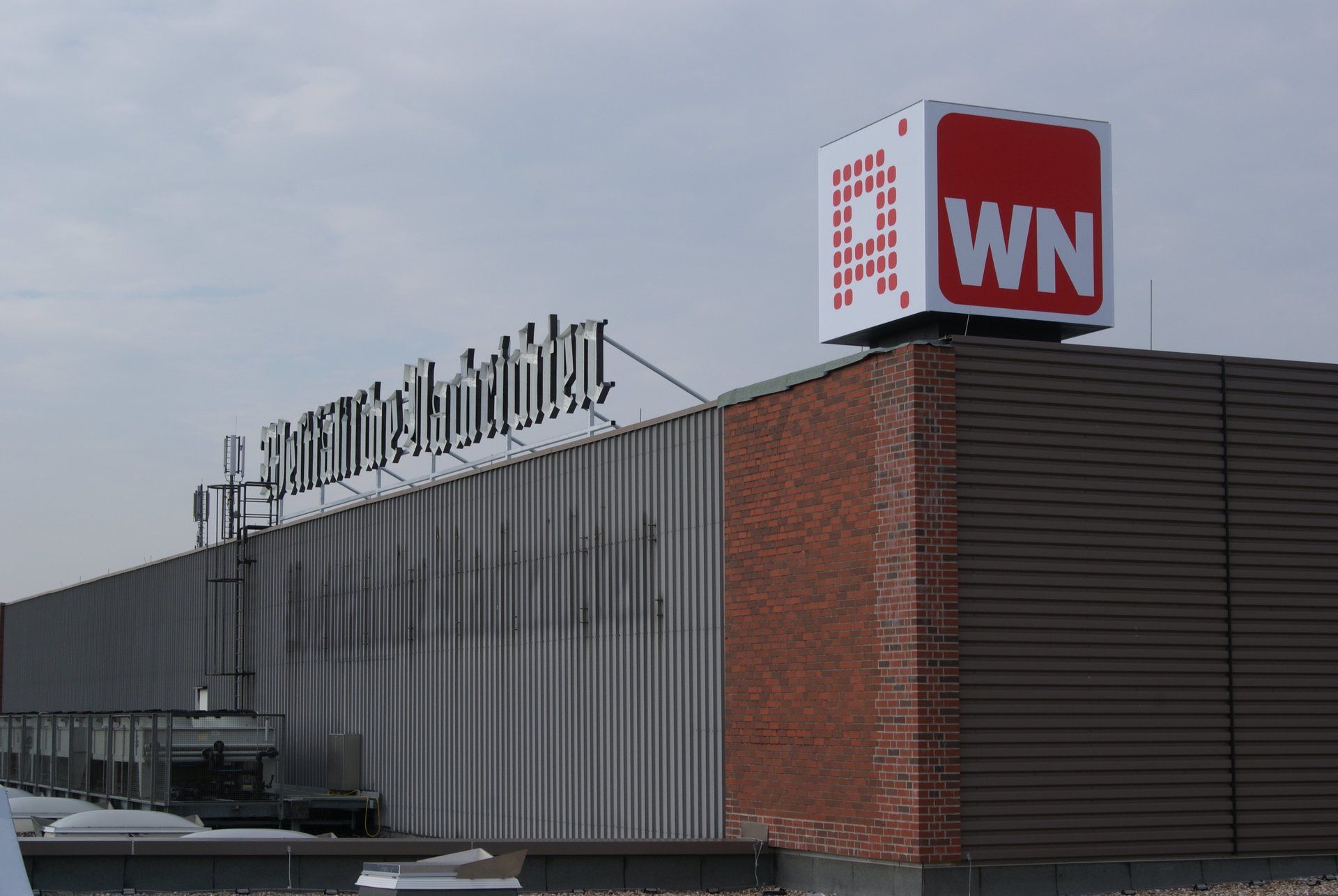 Schild auf dem Dach eines Gebäudes: „WN“-Logo in Weiß auf rotem Hintergrund, neben einem Geschäftsnamenschild.