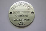 Metallscheibe mit der Gravur „Milwaukee Iron Store, Oldenburg, Harley-Parts and Service“.